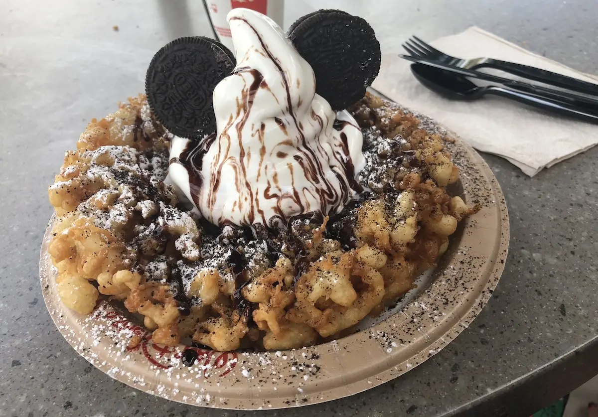 Funnel cake with a large dollop of ice-cream on it and two biscuits that look like Mickey Mouse ears