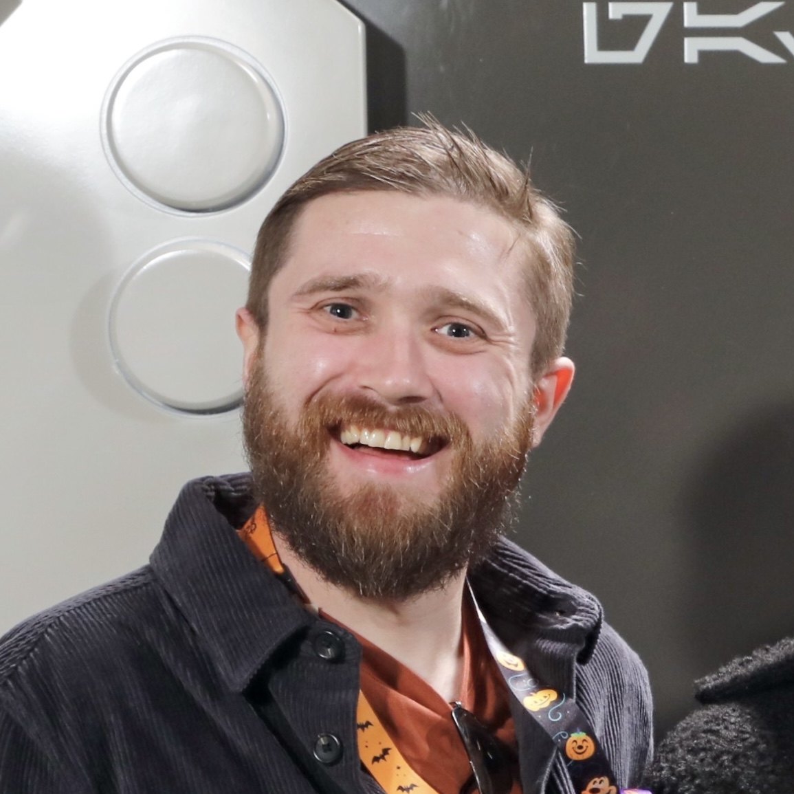 A headshot of Toby Osbourn: a white man with a beard smiling